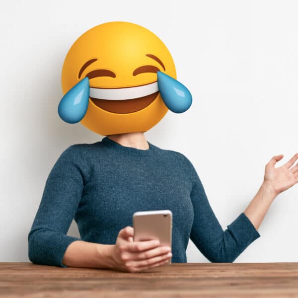 Frau mit Handy in der Hand und Lach-Emoji als Kopf