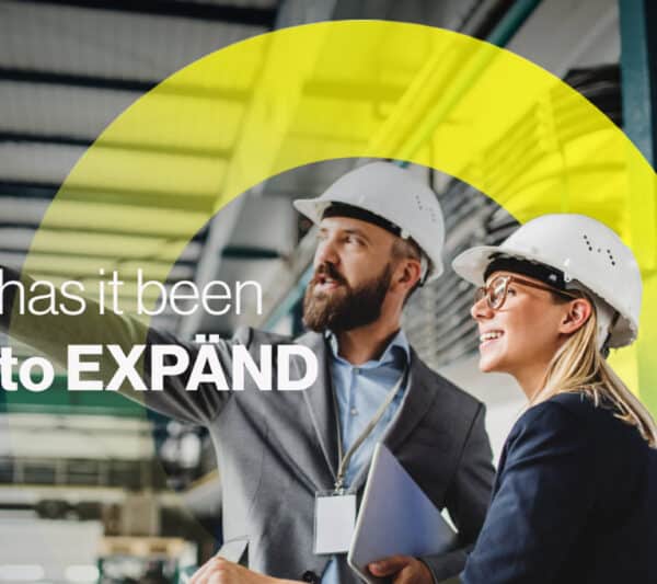 Keyvisual EXPÄND - 2 Personen mit Bauhelmen die auf etwas außerhalb des Bildes zeigen und schauen